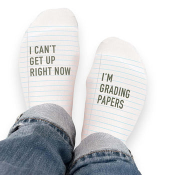 Pair of no-show socks with a black heel and a message on top; I can’t get up right now I’m grading papers.