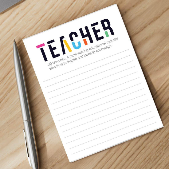 tee-cher notepad and silver pen sitting on a desk