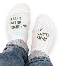 Pair of no-show socks with a black heel and a message on top; I can’t get up right now I’m grading papers.