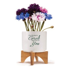 Two-piece bamboo stand with modern white ceramic planter featuring the inspirational message “Our Students Grew Because Of You.” Grows a patriotic mix of flowers.